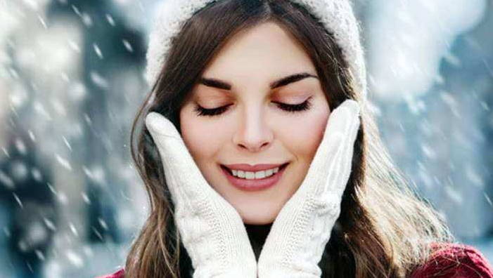 Djevojka s vunenom kapom i rukavicama prekriva obraze rukama dok pada snijeg